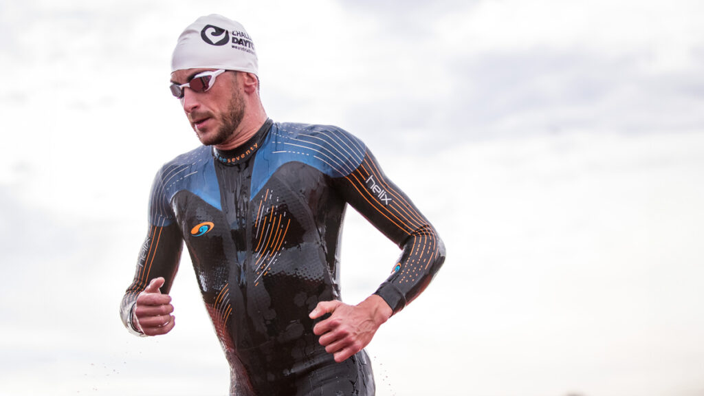 Cody Beals in wetsuit, swim cap and goggles running with clear sky in the background