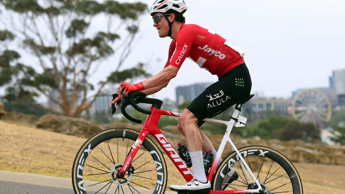 Trainingpeaks And Team Jayco Alula – Sprintcyclingagency Male Cyclist Racing With City In The Background Team Jayco Alula