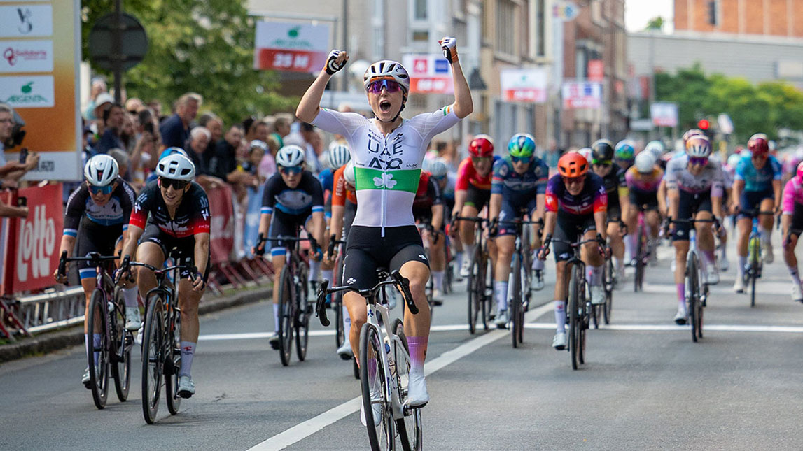 Trainingpeaks And Uae Adq Female Cyclist Crossing The Line In First Place Celebrating With Fists In The Air From Team Uae Adq