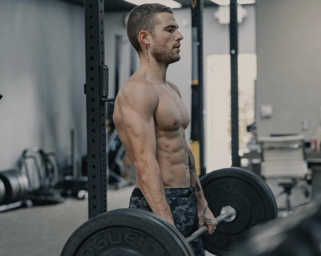 Shirtless male cycling athlete strength training by performing a deadline with a barbell and weights