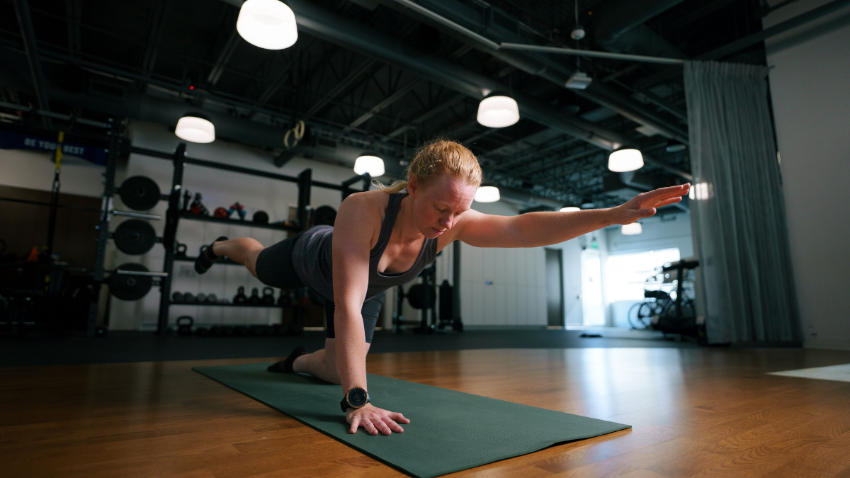 Female Athlete Warming Up For Strength Training In Gym Doing Bird Dog Exercises