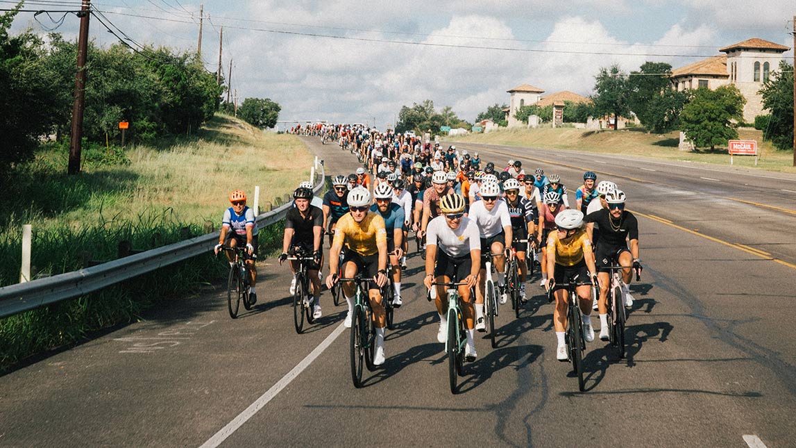 Large Group Of Cyclists Riding Down The Road Together, Led By Team Breakfast Club