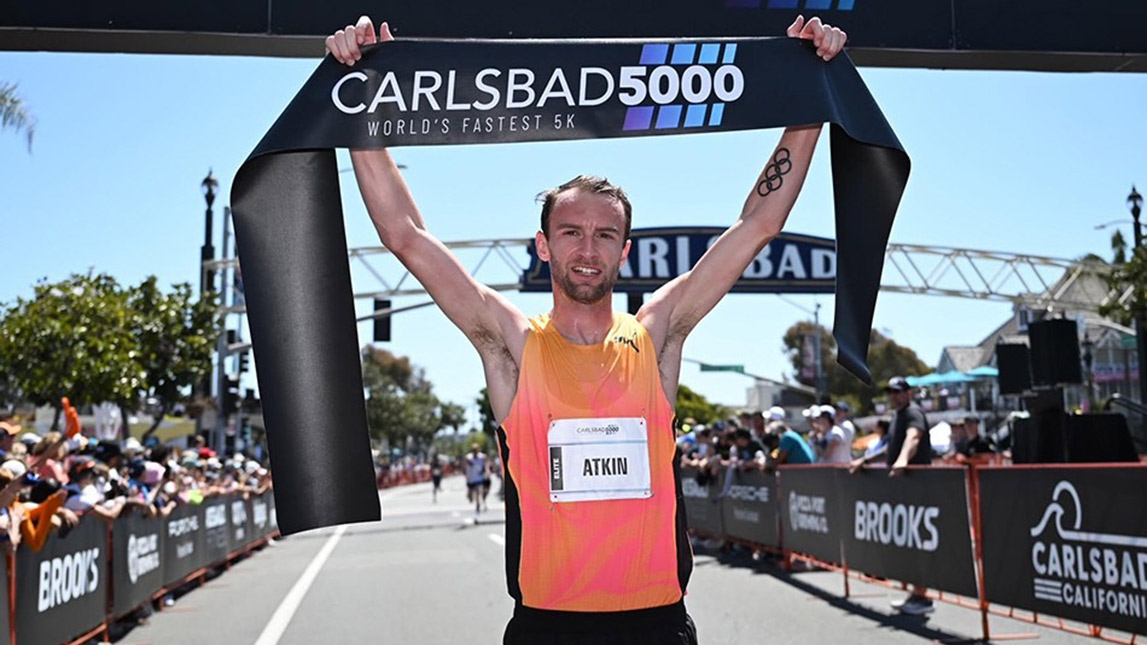 Union Athletics Club And Trainingpeaks Male Runner Holding Carlsbad 5000 Banner Up At Finish Line Union Athletics Club