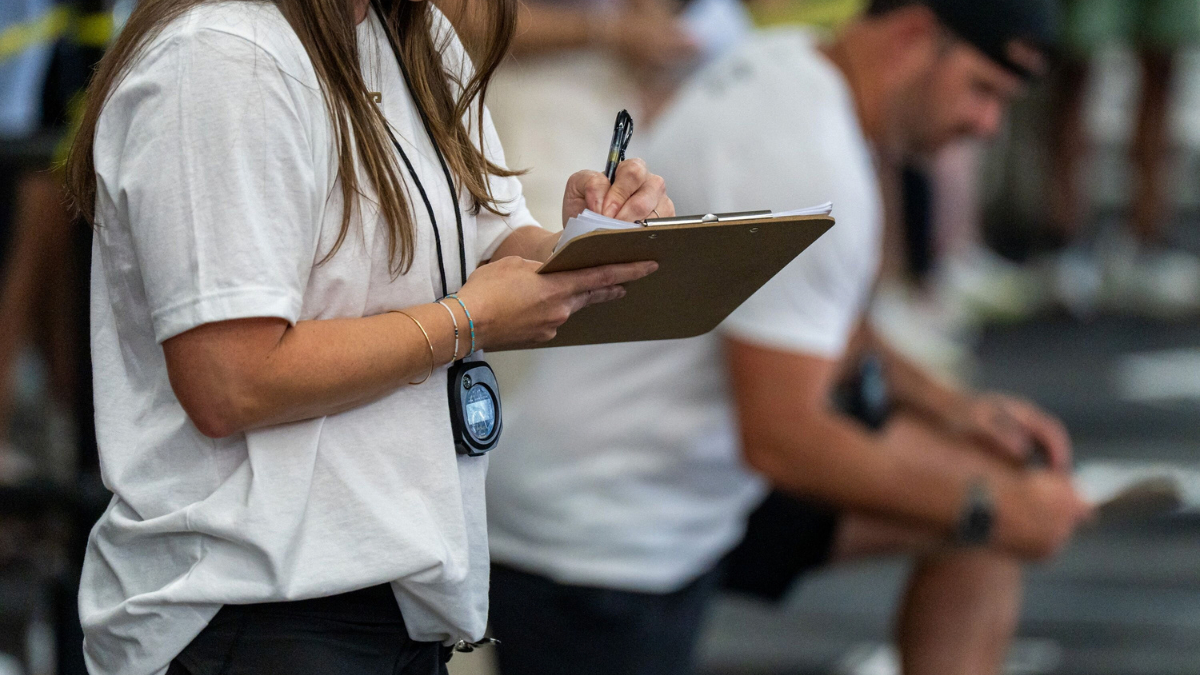 Coaching Systems Coach Wearing A Stopwatch And Writing On Her Clipboard To Assess Athlete Data, Implementing Coaching Systems.